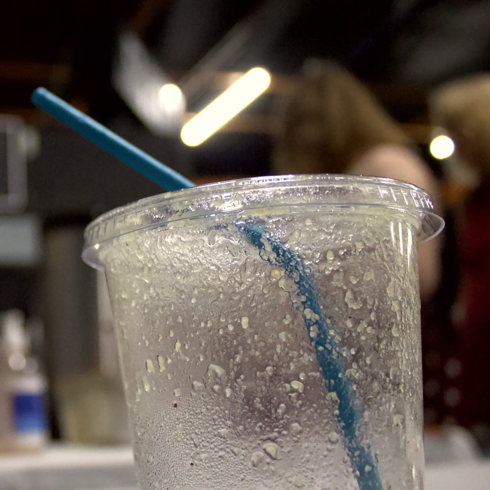 An iced drink in a clear cup, beaded with cold, with a blue straw