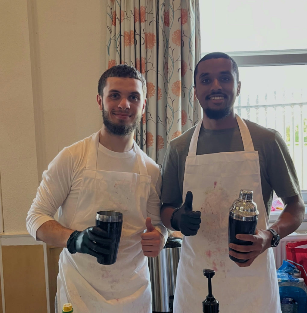 Two people in aprons with their shakers, thumbs up, at the Bristol Muslim Cultural Society event