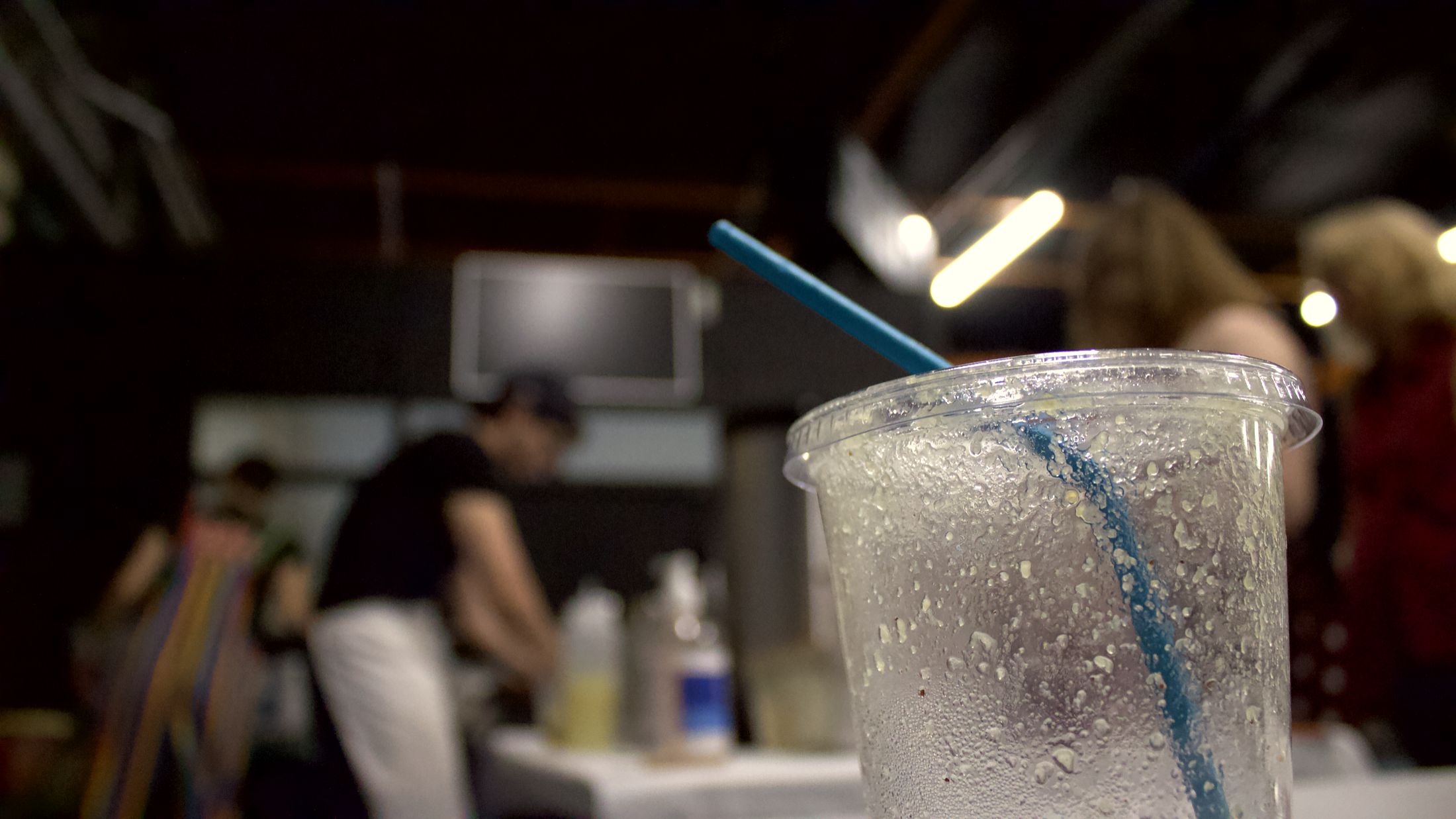 An iced drink in a clear Sanabode cup, beaded with cold, with a blue straw