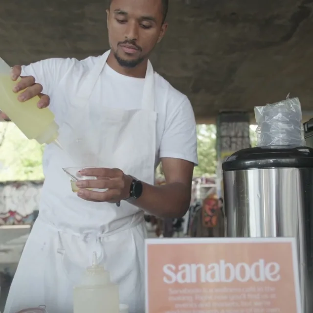 Pouring a lemon blend behind the Sanabode sign