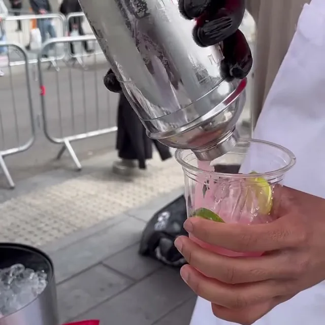 A pink drink with lime being poured from the shaker